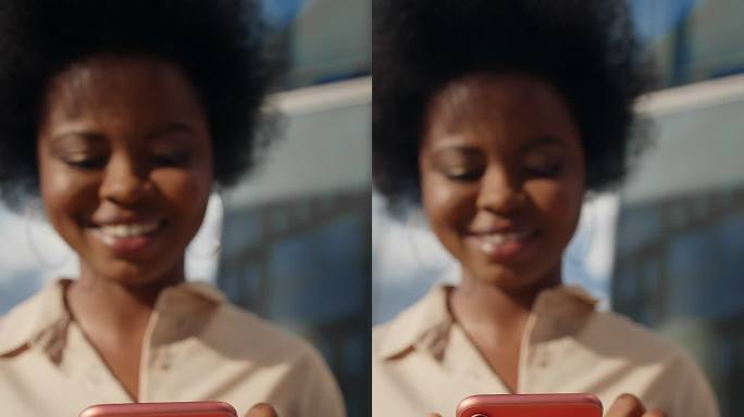 一位身穿米色服装的深色皮肤的漂亮女学生微笑着用红色智能手机发短信，她的脸不在镜头的焦点上，只有手中的