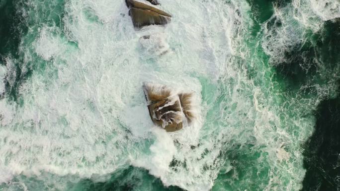 上图是海浪冲刷着旅游目的地的岩石。在国外和海外度假时，无人机鸟瞰碧水和海景。海浪冲击巨石的俯视图