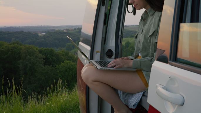 DL黄昏时分，一名年轻女子在乡村的一辆面包车后面使用笔记本电脑