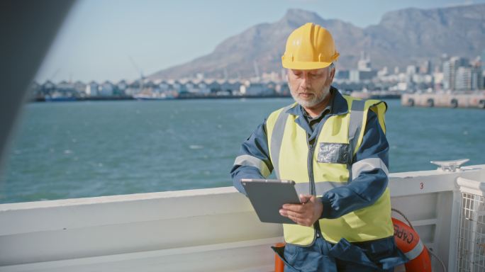 一位成熟的海洋工程师在海上工作时与数字平板电脑进行通信。技术员和维护人员或柴油机机械师从船舶甲板上修