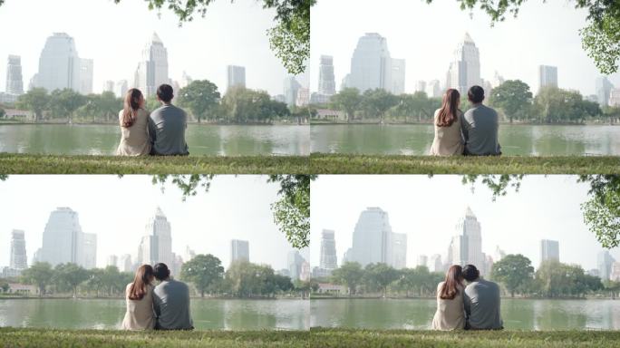 亚洲夫妇坐在绿色的草地上聊天，欣赏美丽的城市景色，人们在城市自然环境中放松身心。