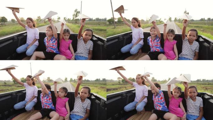 亚洲兄弟姐妹男孩和女孩坐在汽车后备箱里，一起玩玩具纸飞机，在乡村旅行。童年和兄弟姐妹喜欢开车旅行。