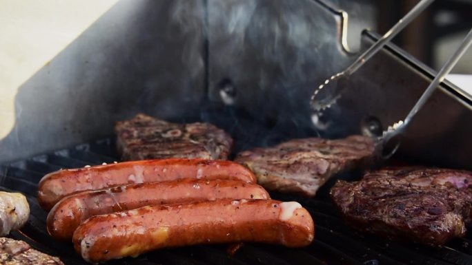 翻肉和热狗用火焰和烟雾烤牛排。家庭烧烤派对。