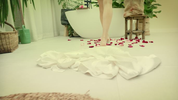 年轻女子走进浴室里郁郁葱葱的绿色花园里的泡泡浴。双腿在玫瑰花瓣上行走的特写