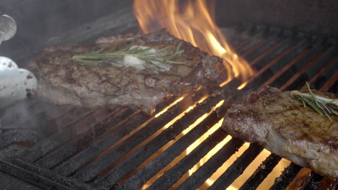 烤肋眼牛排配火焰烧烤，烤架上涂有黄油和迷迭香