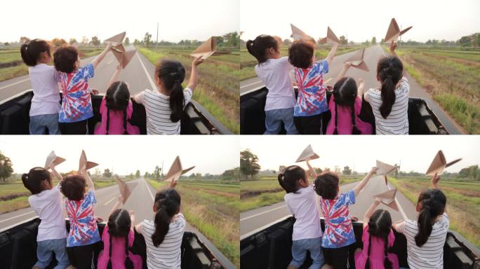 亚洲兄弟姐妹男孩和女孩坐在汽车后备箱里，一起玩玩具纸飞机，在乡村旅行。童年和兄弟姐妹喜欢开车旅行。