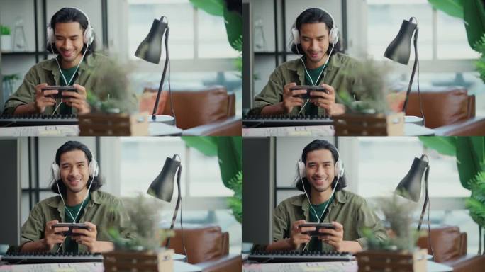聪明的亚洲男性创意自由职业者休闲布呆在家里坐在工作桌前玩流媒体游戏在线戴耳机微笑无忧无虑的面部表情，