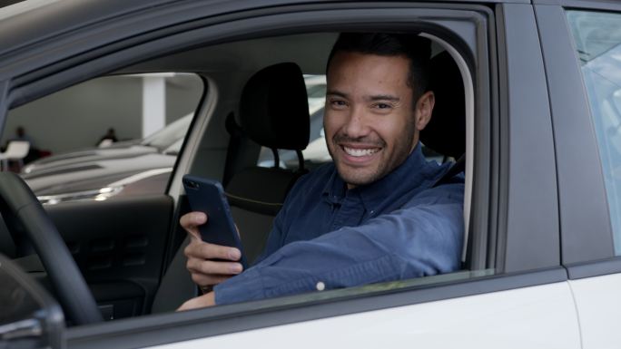 快乐的司机在手机上使用GPS应用程序，看着摄像头微笑