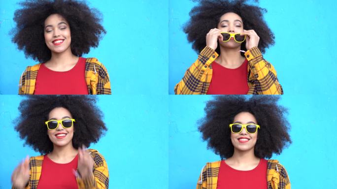 4K视频美丽的非洲裔美国妇女，一头非洲式头发，戴着黄色墨镜，穿着五颜六色的衣服，在蓝色背景下微笑