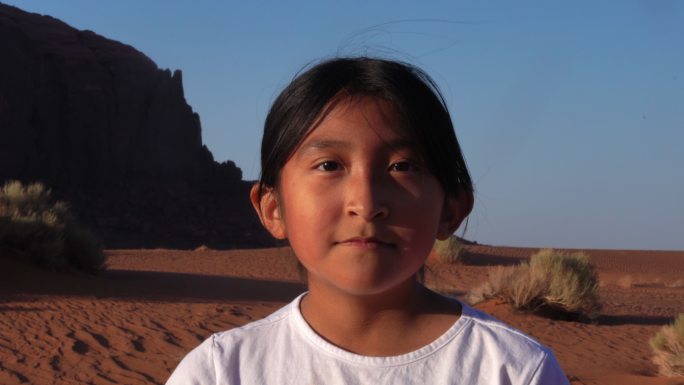在沙丘和红岩悬崖前纪念碑谷附近的年轻女孩视频肖像从中性表情转变为笑容