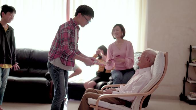 亚洲华人爷爷在家给孙子们发红包。面带微笑的快乐。