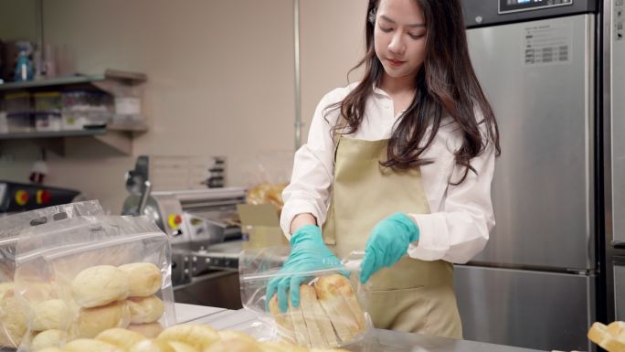 年轻的亚洲女企业家准备和包装新鲜出炉的面包，然后再交付给客户，小企业