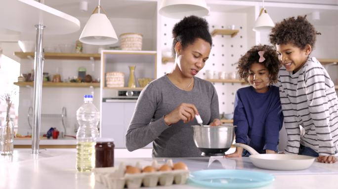 黑人单身母亲和她的孩子们在厨房里做煎饼。