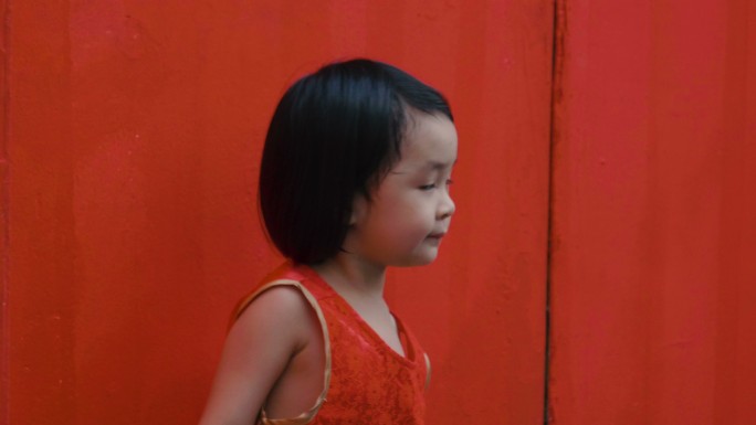 红墙背景上的女婴玩耍无聊倚靠在红色墙壁上