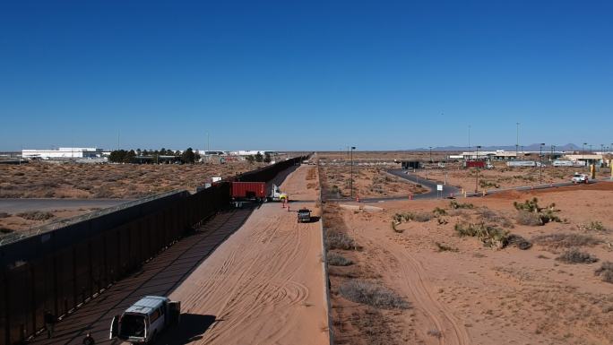 美国、德克萨斯州埃尔帕索附近的墨西哥边境墙和背景中的华雷斯大型半卡车通过边境检查站的低无人机视图