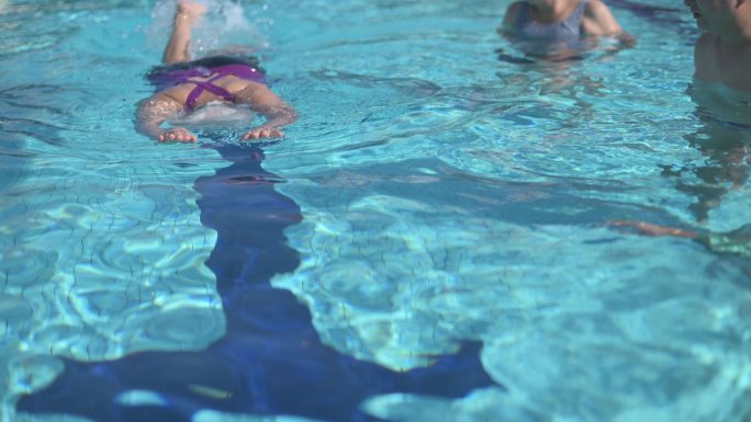 周末上午，亚洲华裔老年女子与退休社区一起在游泳池里向教练学习游泳指导