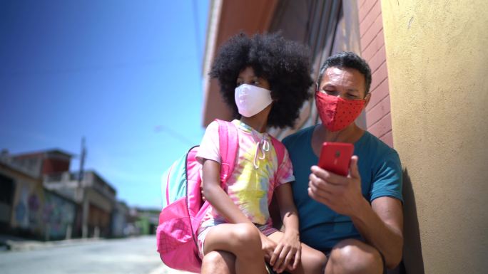父亲和女儿在家门口等校车并使用手机-带口罩