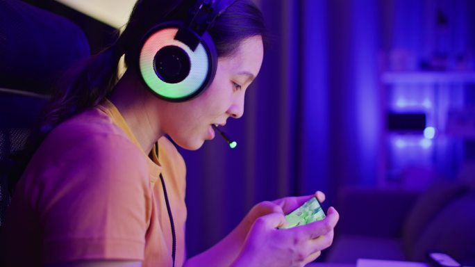 亚洲女人在家里的客厅里用智能手机数码设备玩网络游戏