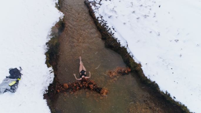 图为冰岛，一位身着泳衣的女士躺在雪景中的温泉中