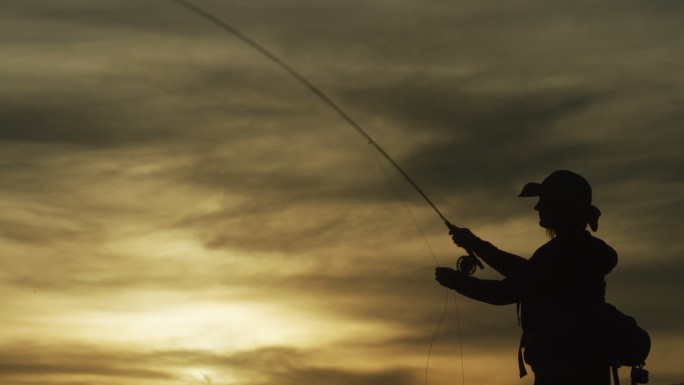 一位身穿剪影的女子在多云的天空下日落时钓鱼