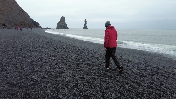 侧视图青少年男孩在冰岛南部Reynisfjara黑沙滩上散步