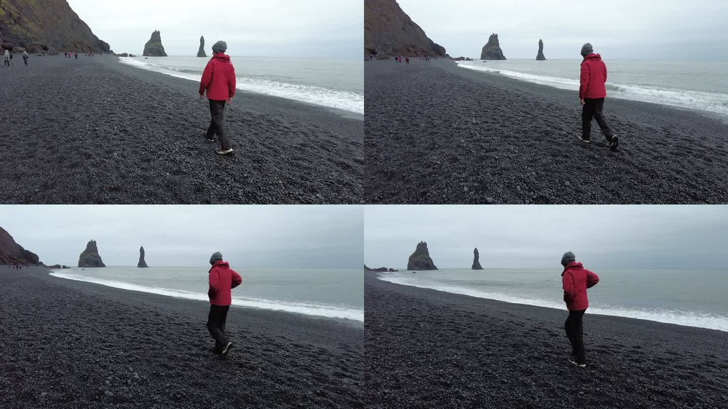 侧视图青少年男孩在冰岛南部Reynisfjara黑沙滩上散步