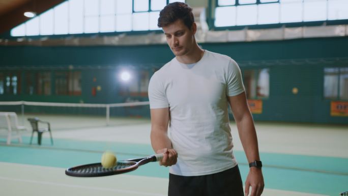 身着网球制服的年轻男教练在球拍上平衡球