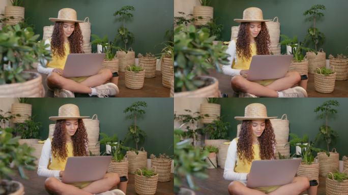 花艺师拿着笔记本电脑，坐在一个充满郁郁葱葱的绿色植物、幼苗和树苗的花园苗圃室里。痴迷于绿色植物的年轻