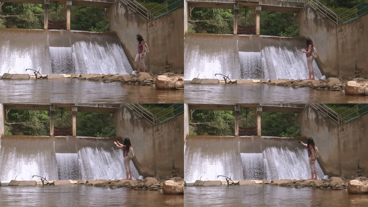 在非城市农业场景中，一位亚洲妇女赤脚走在当地堰前，拍摄瀑布般的漂浮水，泰国北部，心情激动，情绪积极