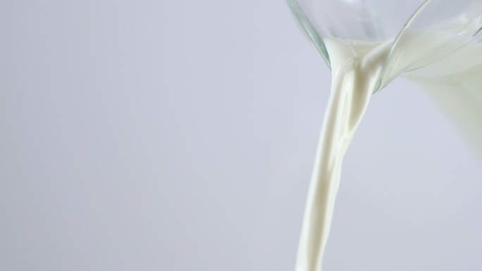 慢镜头：在白色背景下从牛奶罐中倒入牛奶。