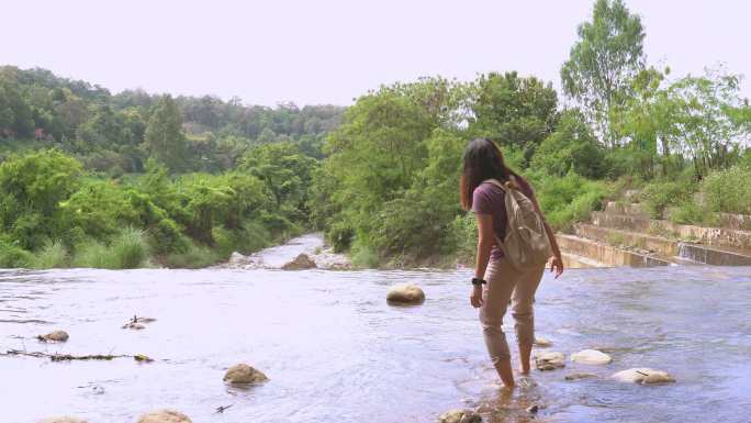 亚洲女子小心翼翼地走到漂浮的水边，看着当地堰前的天然森林，这是一个非城市农业场景，山脉，泰国北部