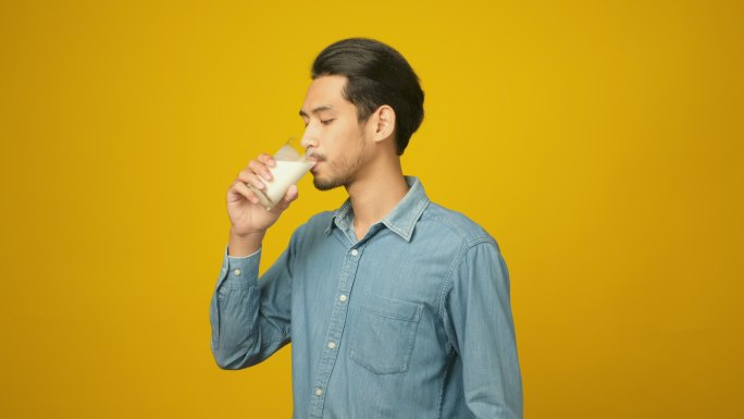 亚洲年轻男子站在孤立的黄色背景下喝牛奶，《食物与饮料》，《人与健康的生活方式》