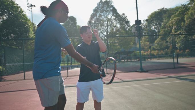 亚洲华人唐氏综合征男子在周末早晨向教练学习打网球