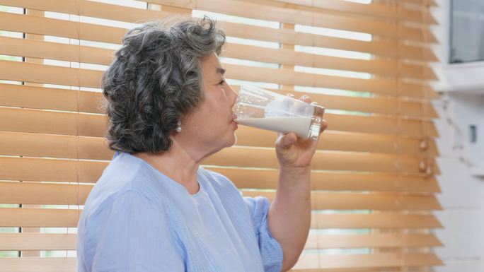 亚洲老年女性在家里的厨房里喝牛奶，退休生活方式，积极的老年健康