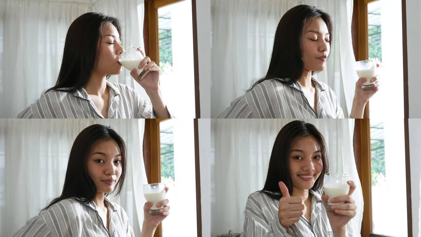 在纯净的早晨，年轻女性的面部表情，喝牛奶，舔嘴唇，竖起大拇指表示状态良好