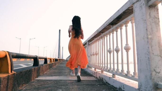 穿着长裙的女孩在桥上奔跑的背影