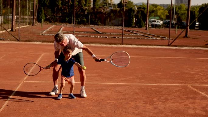 在一次网球练习中，快乐而顽皮的男孩，享受着和爷爷在一起的时光