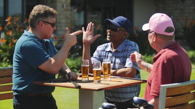 男性高尔夫球手在阳光明媚的露台上击掌喝啤酒