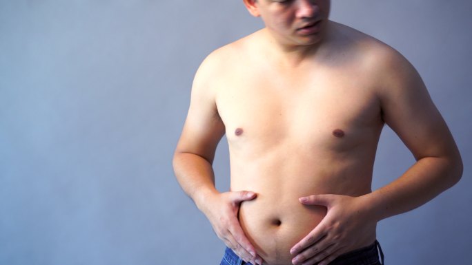 胖子超重，手抱着肥胖的腹部，背景为灰色。