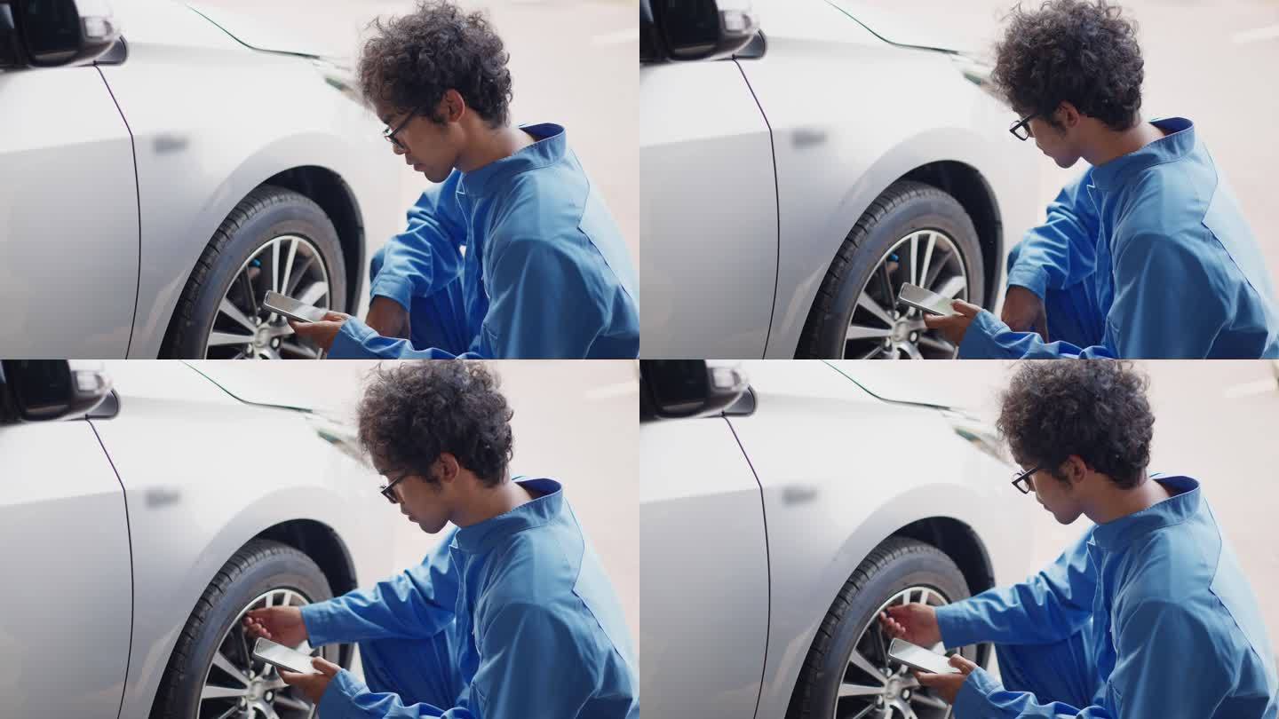 亚洲中年汽车工程师身着蓝色机械连体裤，使用智能手机显示屏检查轮胎气压
