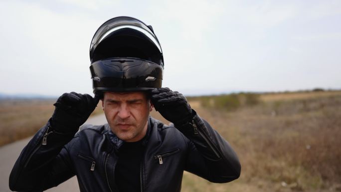 骑车人走向摩托车并戴上头盔