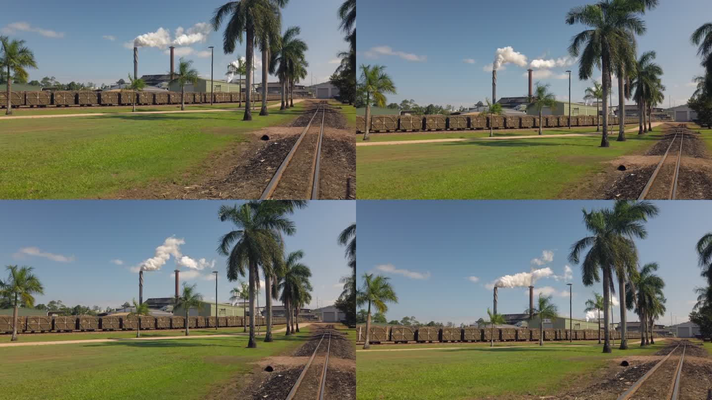 一辆甘蔗火车在铁路交叉口经过一条乡村公路，进入一家工厂