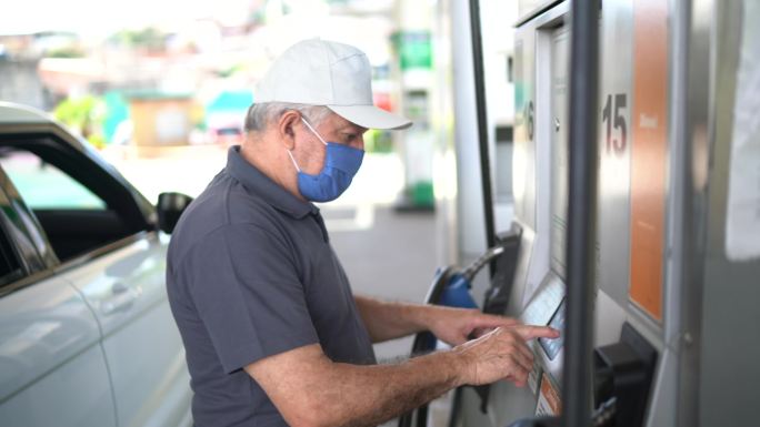 一位戴着口罩的老年男子在加油站给汽车加油的肖像