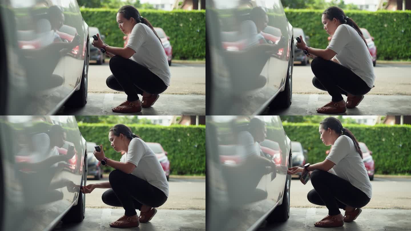 亚洲中年女性使用智能手机显示屏检查汽车轮胎气压，出行前进行汽车检查