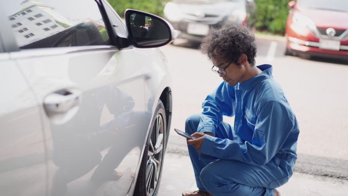 亚洲中年汽车工程师身着蓝色机械连体衣，通过智能手机显示屏检查轮胎气压，家用服务车检查