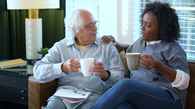 家庭护理人员和老人交谈，在沙发上喝咖啡