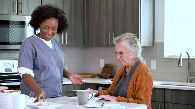 家庭护理员帮助老年妇女在厨房吃饭