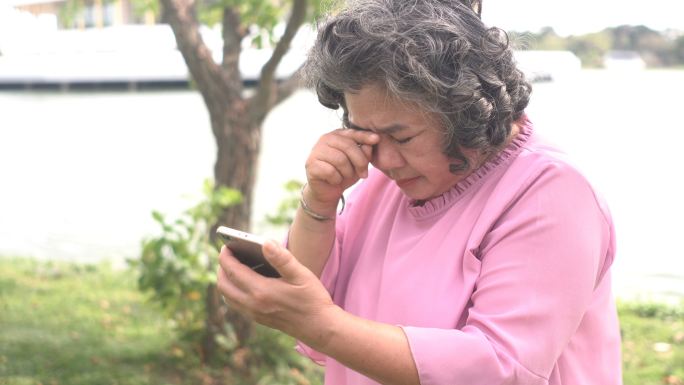 前视图：眼睛有问题的老妇人斜视，很难使用智能手机