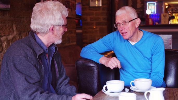 两名老年男子在酒吧边喝咖啡边聊天