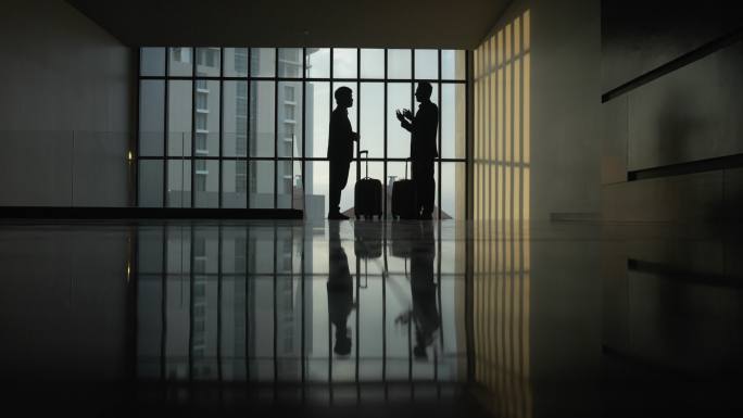 两位商人站在酒店大厅的大全景窗旁握手交谈。